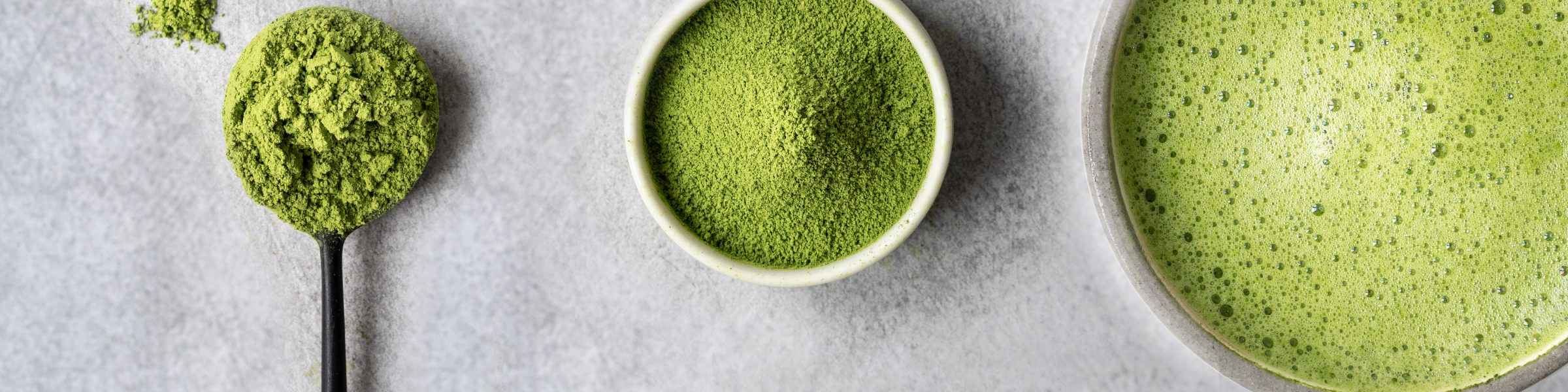 Matcha-Pulver auf einem Löffel, eine Schale mit Pulver und eine Schale mit aufgeschlagenem Matcha